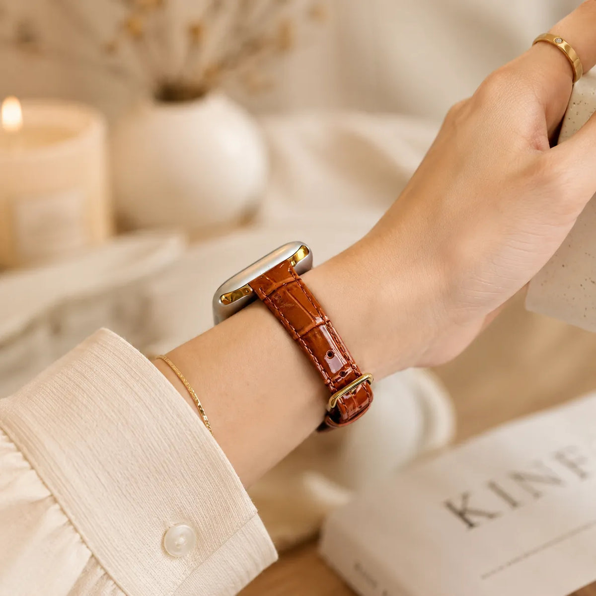Brown textured leather Apple Watch band worn with a cream blouse and gold jewelry